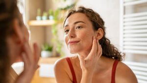 Ragazza allo specchio si spalma la crema per idratare la pelle del viso
